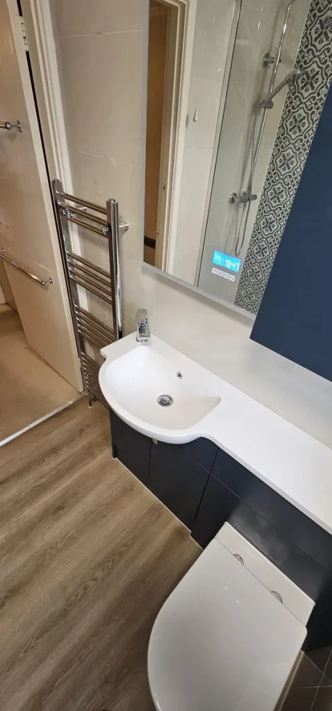 Curved basin on a navy vanity unit with chrome towel radiator and wood-effect floor