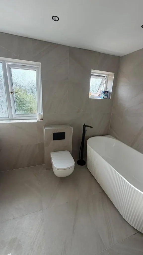 Wall-hung WC, black floor-standing bath tap and fluted bath in large-format stone-effect tiles